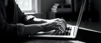 Professional businessman typing on laptop computer in modern office workspace with natural window lighting for remote work and business productivity.