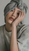 Young Asian woman in gray towel turban after shower touching face with hand in spa wellness skincare routine portrait for beauty and self-care concepts.