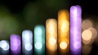 Glowing colorful bar chart made of blurred bokeh lights showing upward trend against dark background with soft defocused circles creating magical atmosphere.