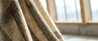 Elegant beige linen curtains with natural texture hanging by bright window creating warm cozy interior atmosphere for home decor and living space design.