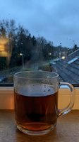 Glass mug of hot tea on wooden windowsill with raindrops on window during cozy evening atmosphere for relaxation and comfort concepts.