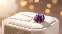 Amethyst crystal cluster pendant on delicate chain displayed on beige jewelry box with warm bokeh lighting, suitable for jewelry retail and luxury product marketing.