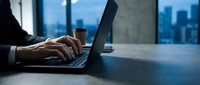 Businessman typing on laptop at dark office desk with city skyline at night, coffee cup nearby, focused work and productivity concept.