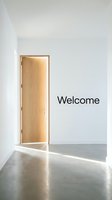 Minimalist white room with an open wooden door letting in warm light and a Welcome sign on the wall, symbolizing new beginnings and opportunity.