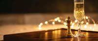 Golden champagne flute and chess king piece on wooden table with warm bokeh lights creating elegant luxury atmosphere for celebration and strategic success.