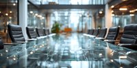 Empty modern corporate boardroom with glass conference table and leather chairs in contemporary office building with natural light.