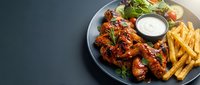Spicy buffalo chicken wings with french fries and ranch dipping sauce served on plate with fresh salad garnish for restaurant menu and food delivery.