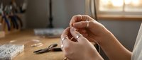 Close-up of hands threading a needle in bright natural light, preparing for sewing or embroidery work in cozy home crafting space.