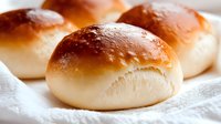 Fresh baked golden brown dinner rolls with soft fluffy texture on white cloth, perfect for bakery menu and food photography projects.