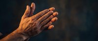Elderly hands pressed together in prayer or meditation gesture against dark background with warm golden lighting creating spiritual atmosphere.