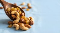 Mixed nuts spilling from wooden spoon on light blue surface. Healthy snacking, protein-rich foods, natural nutrition concept for cooking and dietary content.