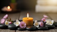 Spa wellness scene with burning honeycomb candle and cherry blossom flowers on black stones for relaxation and meditation therapy treatment.