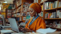 African woman in bright orange headwrap and traditional attire working on laptop in library setting, wearing turquoise jewelry. Modern professional in cultural dress.