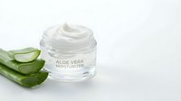 Open jar of aloe vera moisturizer cream with fresh green aloe leaves on clean white background for skincare and cosmetic product advertising.