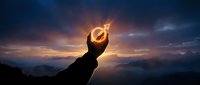 Hand holding glowing male gender symbol against dramatic sunset sky with mountains silhouette representing masculinity and identity concepts.