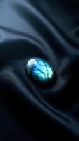 Polished labradorite gemstone with brilliant blue flash resting on luxurious dark silk fabric creating elegant waves and shadows for jewelry design concepts.