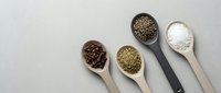 Assorted spices and seasonings in wooden spoons arranged on neutral background for culinary cooking and food preparation concepts.