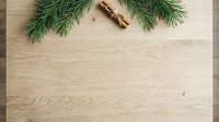 Evergreen branches with cinnamon sticks arranged on light wooden surface, offering festive holiday styling for seasonal marketing and decorative projects.