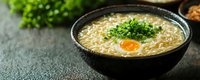 Asian ramen noodle soup with egg yolk and green onions in black bowl on dark stone surface. Traditional Japanese comfort food for restaurant menus.