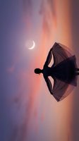 Silhouette of woman dancing with flowing fabric against dramatic sunset sky with crescent moon. Graceful movement and artistic expression in twilight atmosphere.