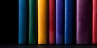 Colorful book spines arranged in row against black background create vibrant rainbow pattern, highlighting texture and minimal composition for literary concepts.