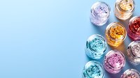 Colorful metallic foil glitter in glass jars arranged on pastel blue background with copy space. Sparkly makeup and nail art decoration materials.