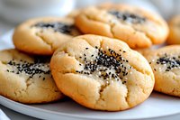 Fresh baked butter cookies with black sesame seeds on top, served on white plate. Close up view shows soft, crackled texture of homemade sweet treats.
