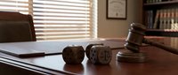 Wooden gavel and scales of justice on polished desk in law office with books and window blinds creating professional legal atmosphere.