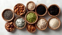 Assortment of healthy seeds, nuts and superfoods in wooden bowls on light background, including almonds, chia, pumpkin seeds and oats.