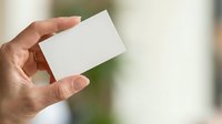 Person holding blank white business card in hand against blurred background, suitable for branding and corporate identity mockups.