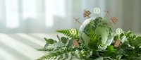 Green glass globe with renewable energy icons surrounded by fresh fern leaves on wooden surface representing sustainable development and eco-friendly solutions.