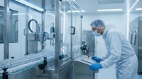 Pharmaceutical scientist in protective gear operating automated production equipment in sterile cleanroom manufacturing facility for drug development.