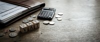 Business financial planning concept with calculator, coins, wooden VAT blocks and documents on rustic wooden desk for accounting and tax preparation.