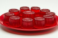 Red gelatin desserts arranged on round plate, individual portions with decorative ridged shapes. Sweet treats showcase translucent texture and vibrant color.