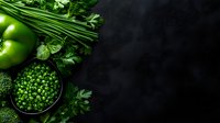 Fresh green vegetables and herbs arranged on dark background with copy space, featuring green peas, bell peppers, parsley and chives for healthy eating concept.
