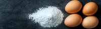 Fresh brown eggs and white flour powder scattered on dark slate surface for baking and cooking preparation in kitchen.