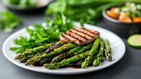 Grilled asparagus spears and meat steak on white plate with fresh herbs. Healthy low carb dinner with green vegetables and protein. Clean eating concept.