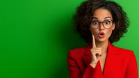 Young mixed race businesswoman with curly hair and glasses showing silence gesture with finger on lips against green background, wearing red blazer.