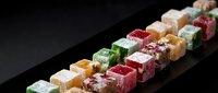 Assorted colorful Turkish delight confections arranged in rows on dark surface, traditional Middle Eastern sweets with various flavors and textures.