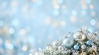 Shiny silver and blue ornaments with metallic accents nestled in frosted evergreen branches against a soft bokeh background, suitable for holiday and seasonal marketing materials.