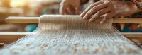 Traditional weaving process on wooden loom showing artisan hands working with natural yarn threads in warm sunlight, closeup panoramic view of textile craftsmanship.