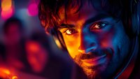 Young bearded man with intense gaze illuminated by dramatic neon lighting in blue and orange colors, wearing headphones against dark background with bokeh effects.