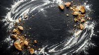 Overhead view of golden baked cookies and flour swirls on dark slate surface, perfect for bakery, recipe, and food blog designs.