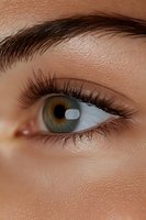 Close-up macro shot of green-brown eye with long eyelashes and defined eyebrow showing natural skin texture and detail. For beauty, cosmetic and medical concepts.
