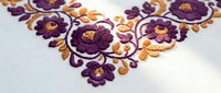 Traditional floral embroidery with purple and orange flowers on white fabric showcasing intricate needlework and decorative stitching patterns.