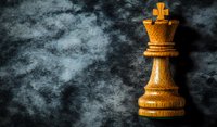 Wooden chess queen piece on dark textured background with dramatic lighting and smoke effect, symbolizing strategy and leadership in business and game.