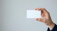 Hand holding blank white business card against neutral gray background, suitable for branding, corporate identity, and marketing mockup designs.