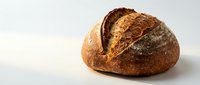 Freshly baked artisan sourdough bread loaf with golden crust and rustic scoring on clean white background for bakery marketing and food photography.