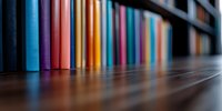 Colorful book spines lined up on wooden shelf with selective focus creating depth effect, multicolored blurred background for education and library concepts.