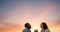 Young couple holding hands against dramatic sunset sky with warm orange and pink hues, expressing love and connection during golden hour for romantic occasions.